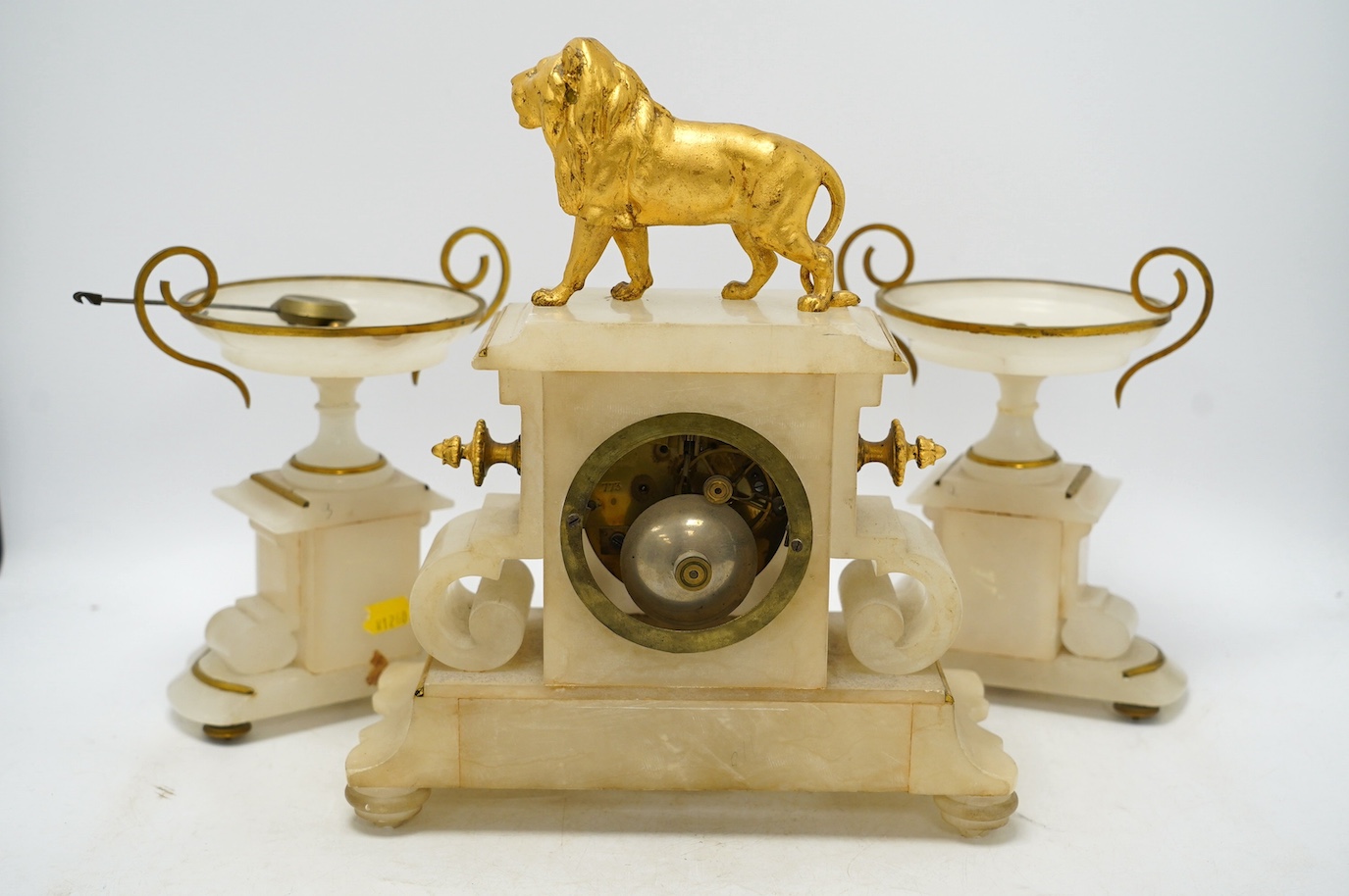 An early 20th century alabaster and gilt metal clock garniture with enamel panels, surmounted with a lion, with pendulum, no key, clock 30cm high. Condition - poor